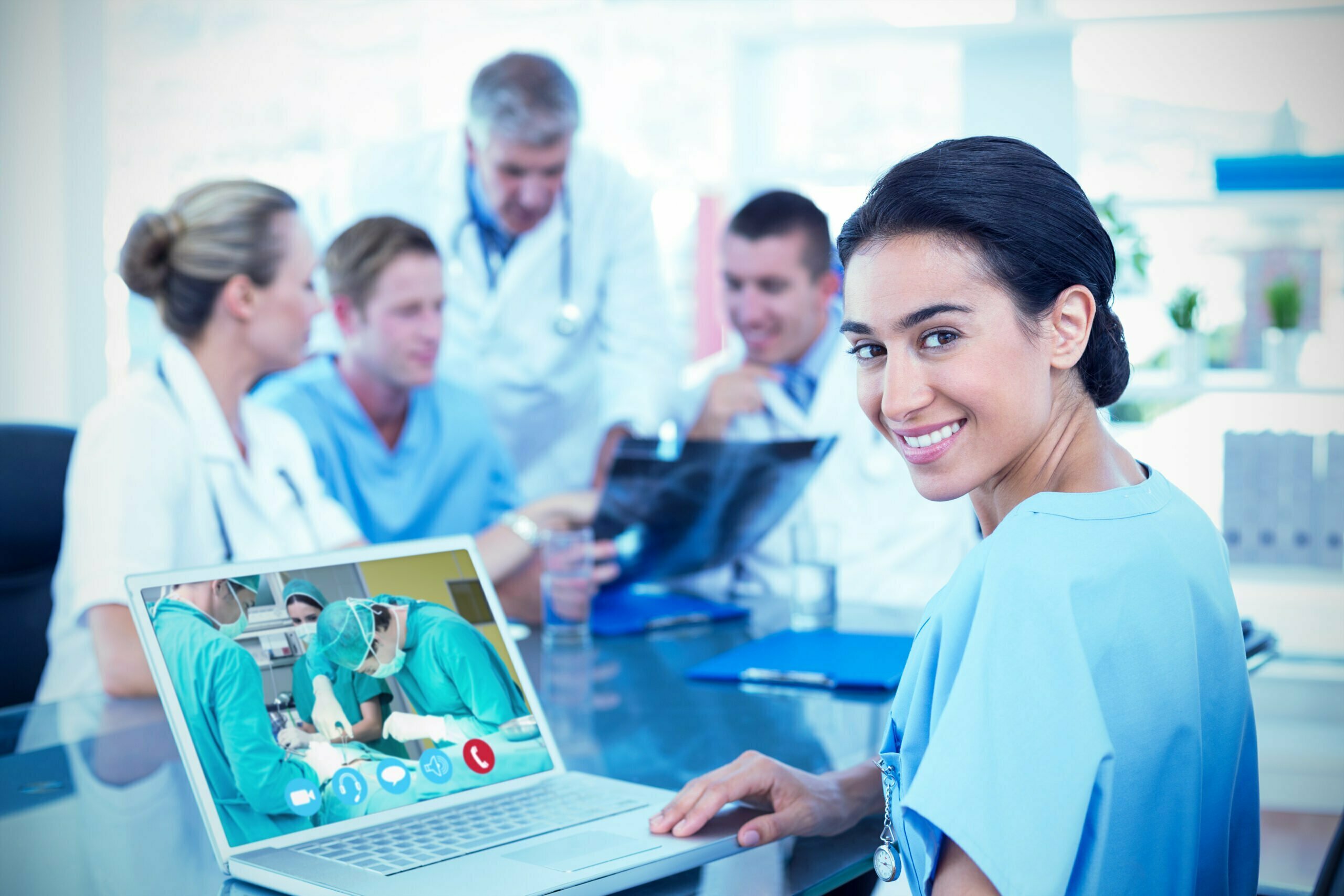 Beautiful smiling doctor typing on keyboard with her team behind against view of video chat app